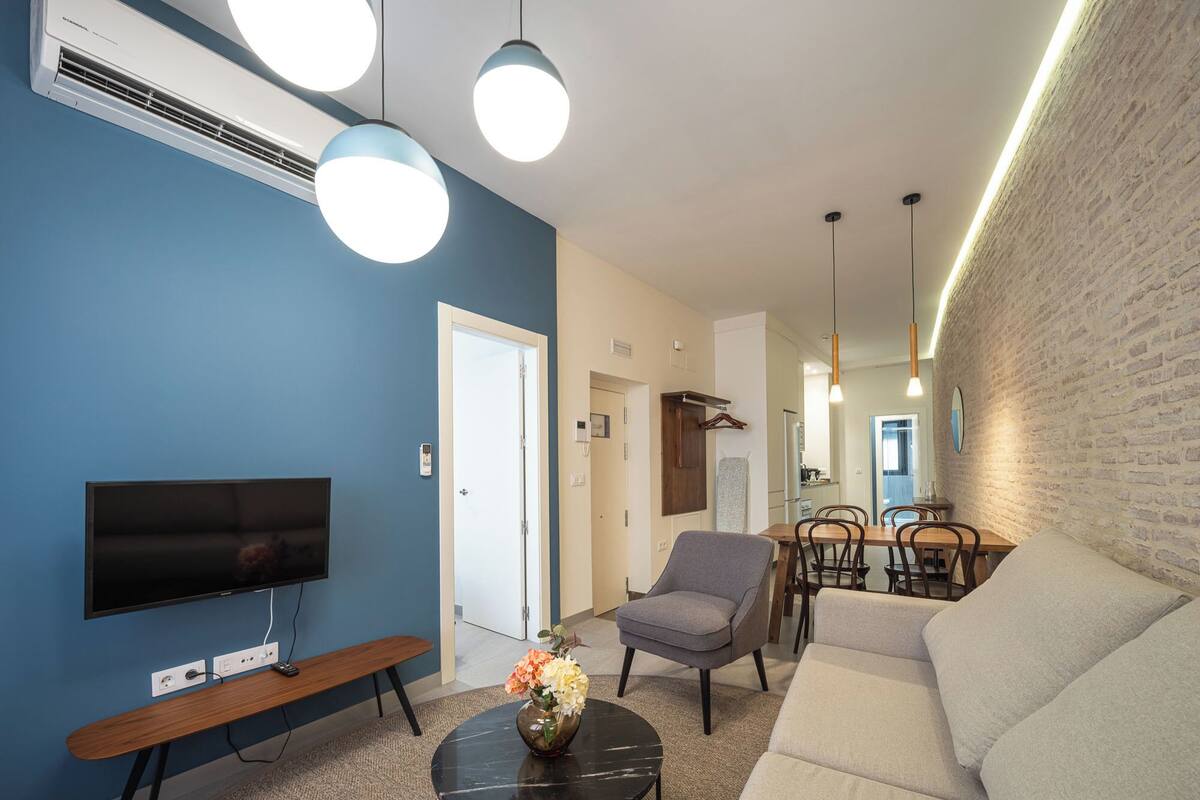 A modern living room with a flat-screen TV, seating, a coffee table, and pendant lights.