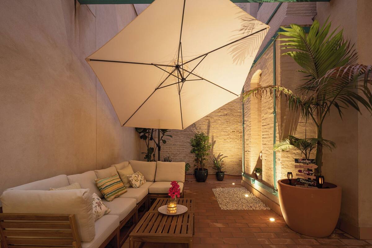 A cozy patio with a sofa, a wooden table, and a large umbrella providing shade.