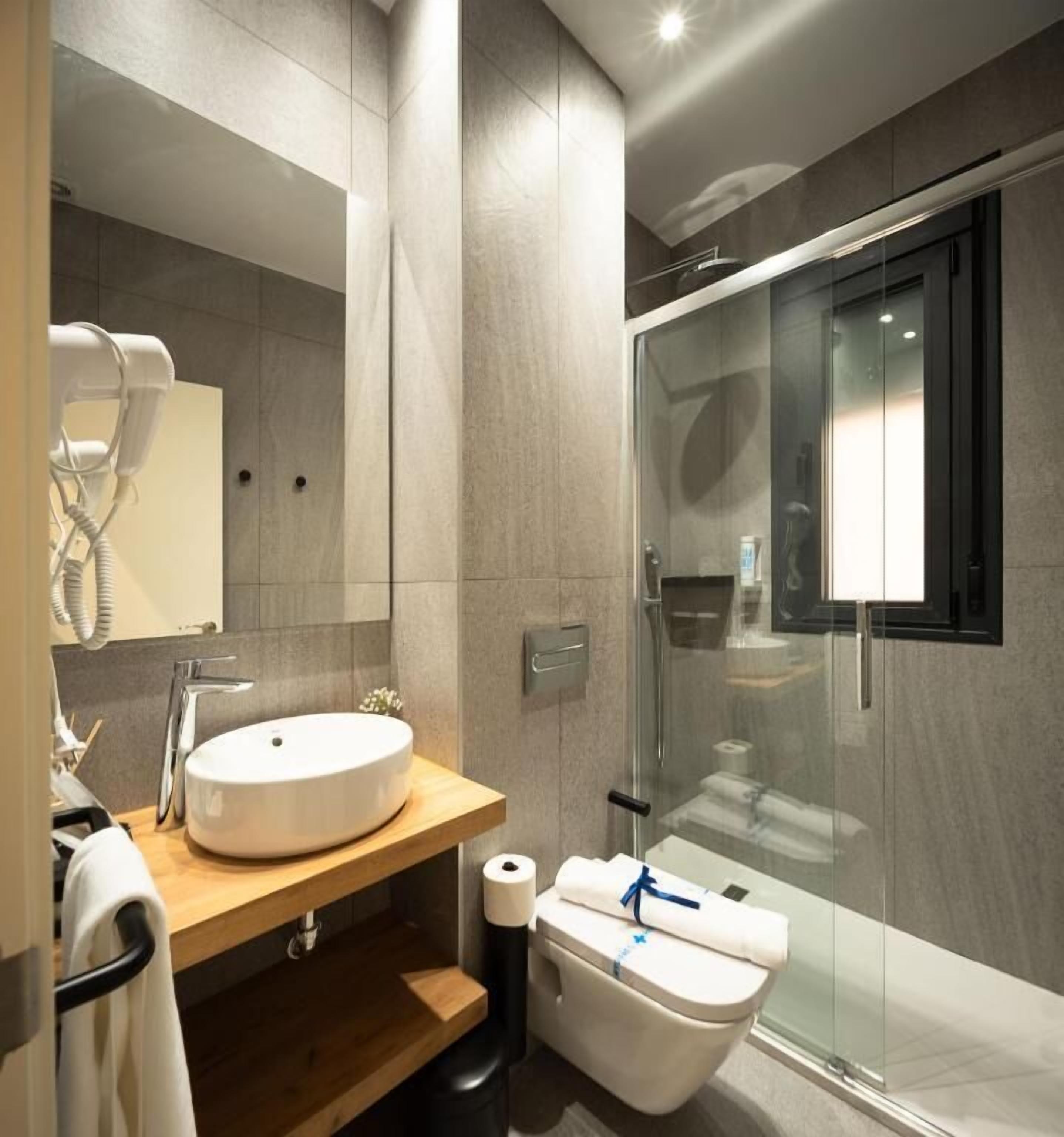 A modern bathroom with a round sink, a hairdryer, a glass shower enclosure, and a toilet.