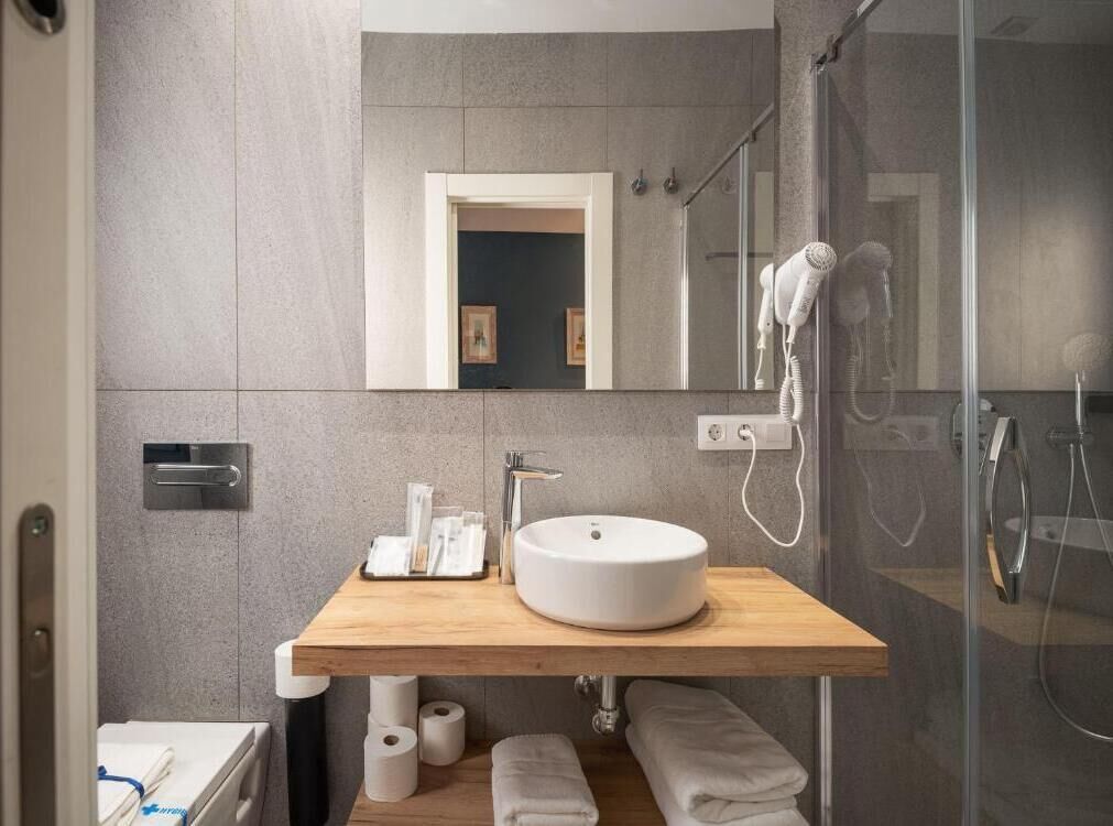 Un baño moderno con tocador de madera, un lavabo redondo, un espejo, un secador de pelo y una zona de ducha.