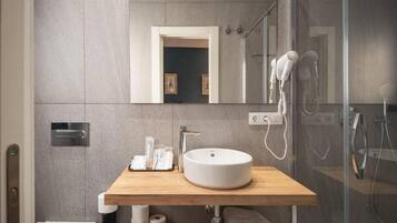 Un baño moderno con tocador de madera, un lavabo redondo, un espejo, un secador de pelo y una zona de ducha.