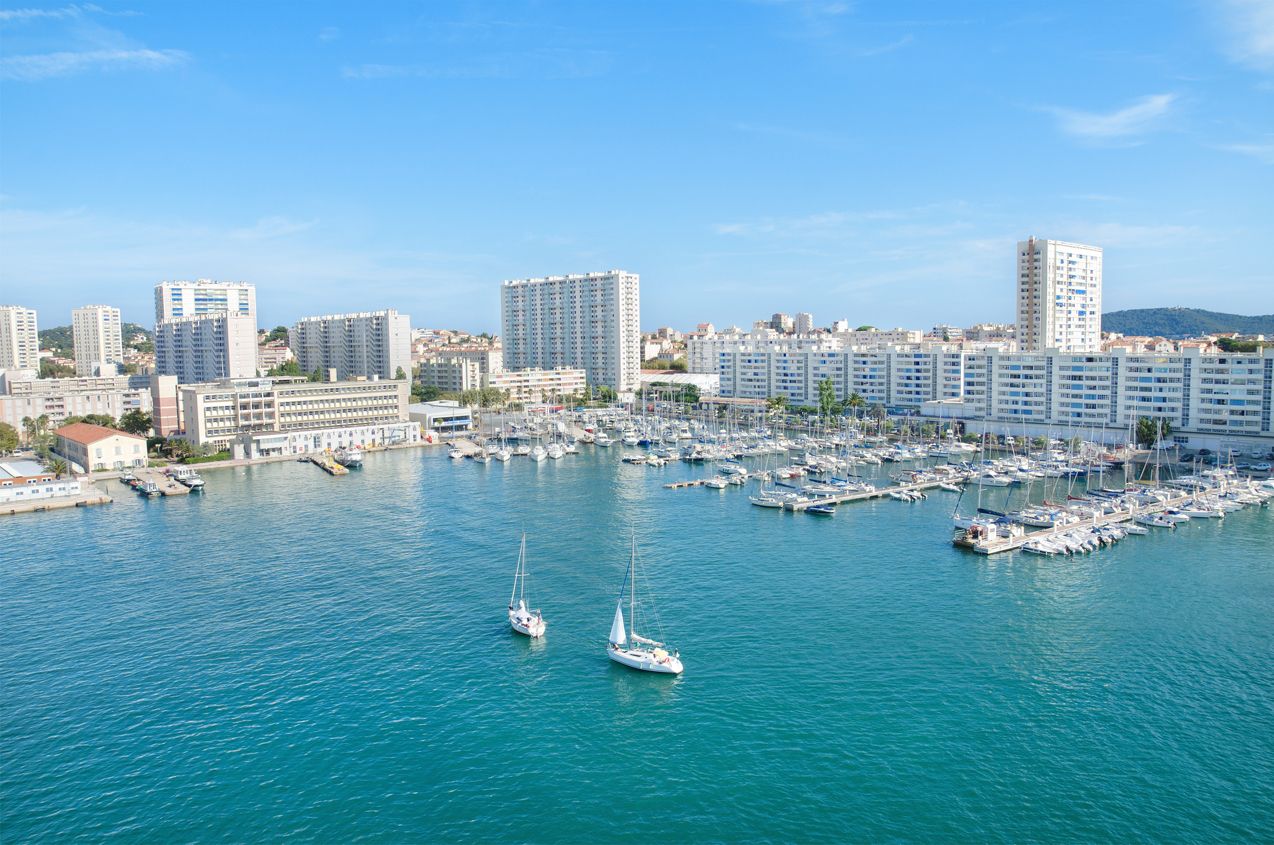 A marina with numerous boats docked, surrounded by high-rise buildings.