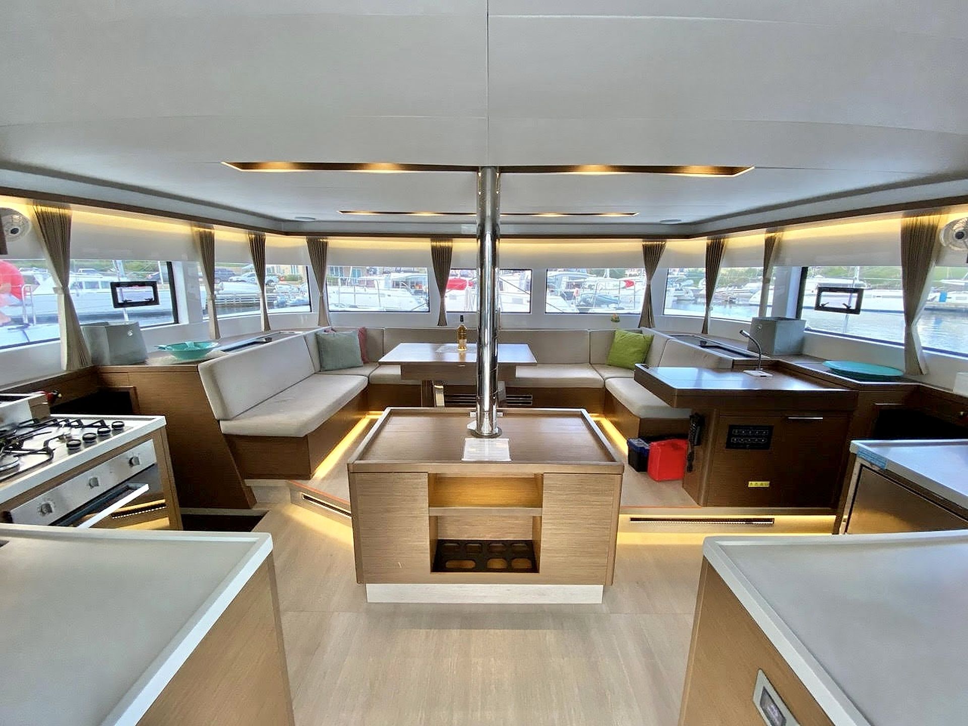 A modern interior with a central seating area, a kitchen with a stove, and large windows offering views of the marina.