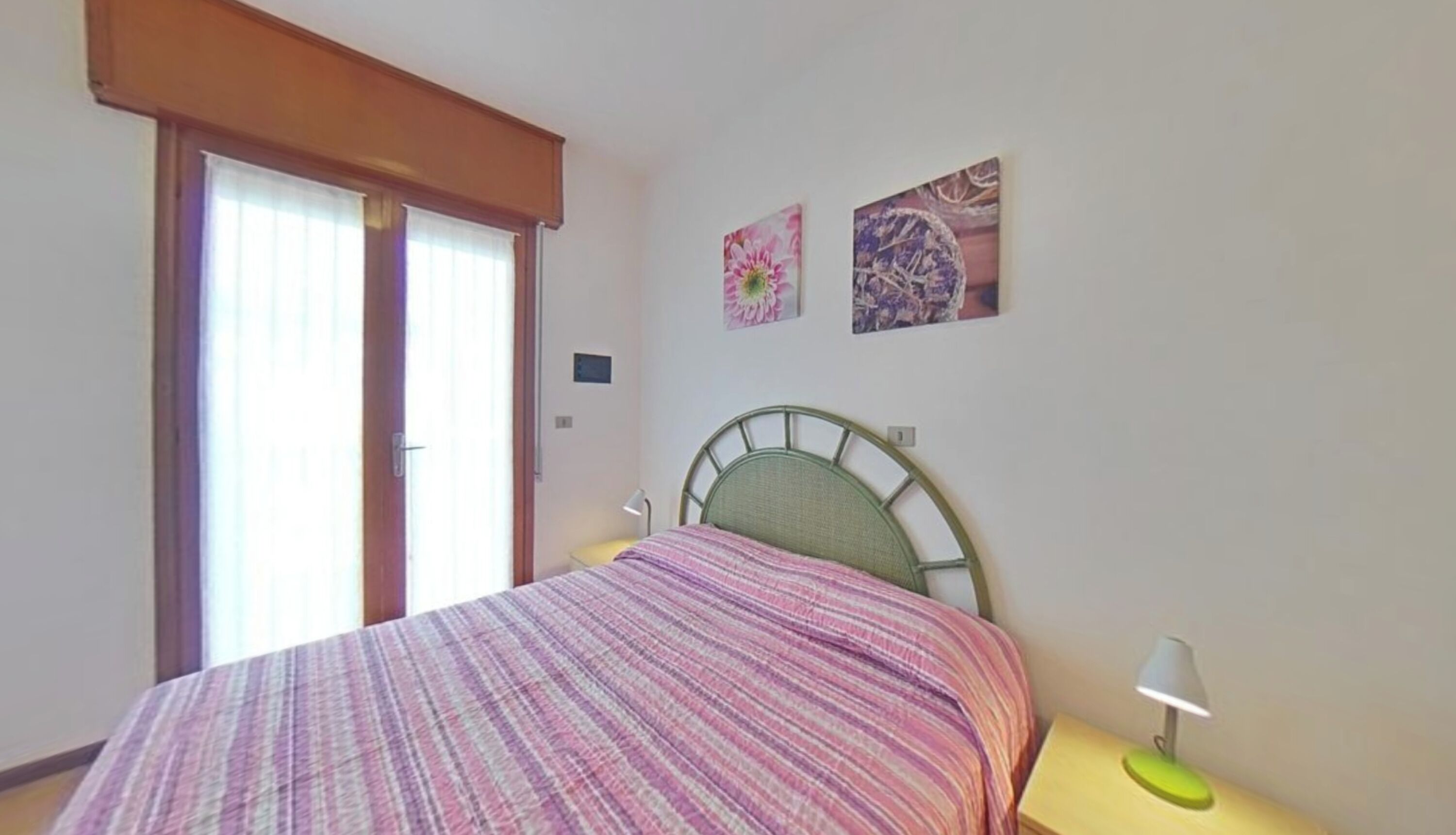 A bedroom with a bed, a window with curtains, a bedside lamp, and two wall-mounted pictures.