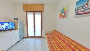 A room with a television, a sofa, a cabinet, a door, and two wall paintings. - Great Stay in a Prime Location (Lignano Sabbiadoro)