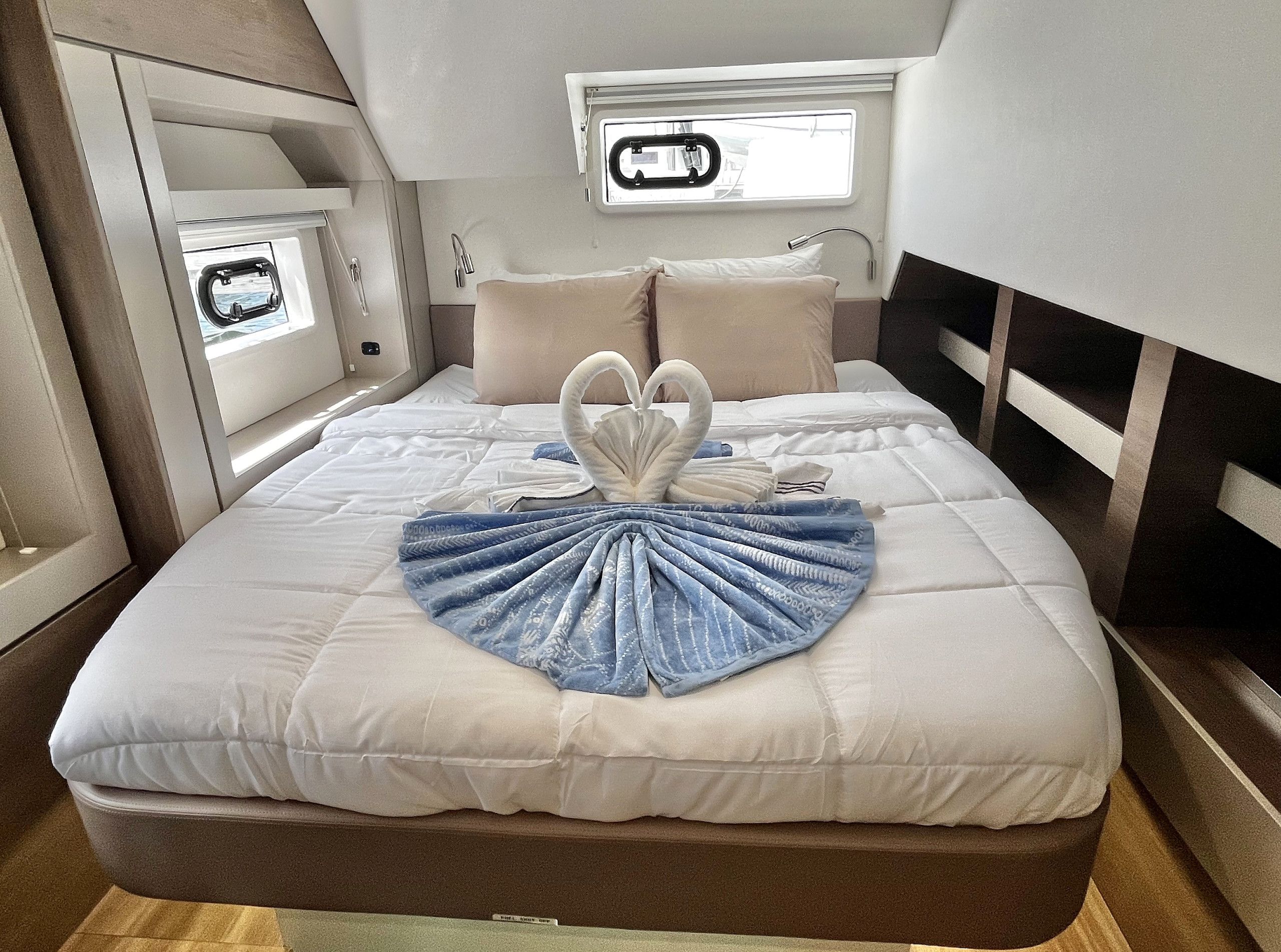 A neatly made bed with a swan-shaped towel arrangement, a window with a view, and a small bedside table with a lamp.