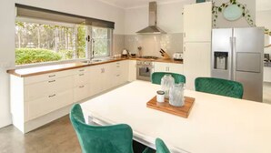 Una cocina moderna con armarios blancos, un refrigerador de acero inoxidable y un comedor con una mesa blanca y sillas verdes.