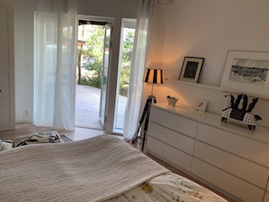 A bedroom with a bed, a dresser, a lamp, and a view of the outdoors.