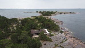 A coastal property with a house surrounded by dense forest, a rocky shoreline, and a view of the sea.