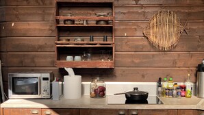 A kitchen with a microwave, a rolling pin, a jar of pickles, and a pot on the counter.