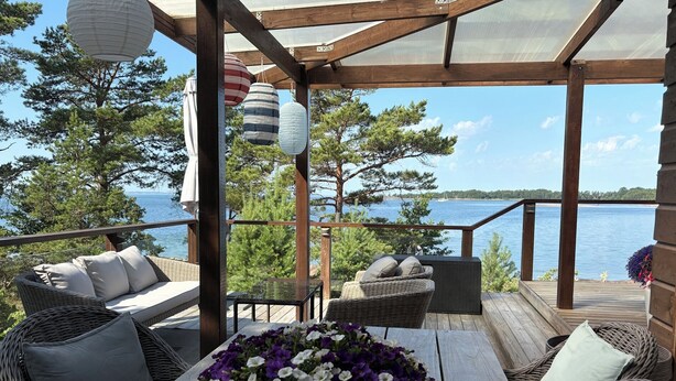 A wooden deck with wicker furniture, a table with a flower centerpiece, and a view of the water.