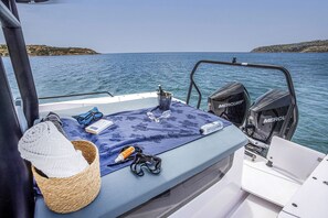 Het dek van een boot met een blauwe handdoek, een gevlochten mand, zonnebril, een boek en een fles zonnebrandcrème.