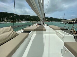 Ein Bootsdeck mit Sitzbereichen, einem Steuer und Blick auf den Hafen sowie Hügel im Hintergrund.