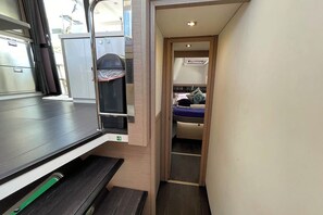 Ein kompakter Raum mit einem Bett, einer kleinen Küchenzeile und einem Fenster.