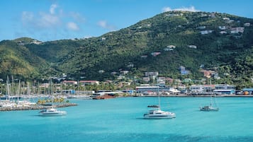 A coastal marina with multiple sailboats docked, surrounded by a hilly landscape with buildings.