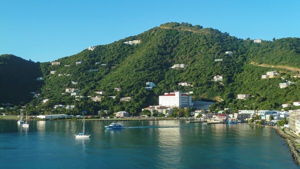 Une ville côtière avec des bâtiments construits sur une colline, un port de plaisance rempli de bateaux et un ciel dégagé.
