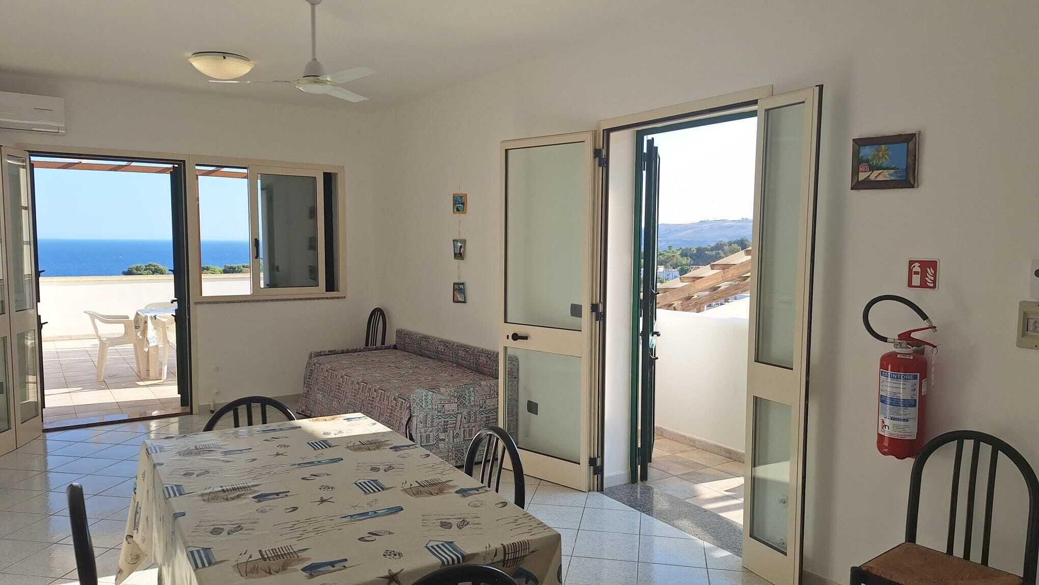 Una habitación con una mesa de comedor, sillas, un sofá, un ventilador de techo y un extintor.