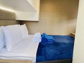 A bed with white bedding and a blue blanket, a wooden headboard, and a wall-mounted light fixture. - Caribbean Dream: Sun-soaked Sailing Adventure from Tortola, Islas Vírgenes Británicas (Road Town)