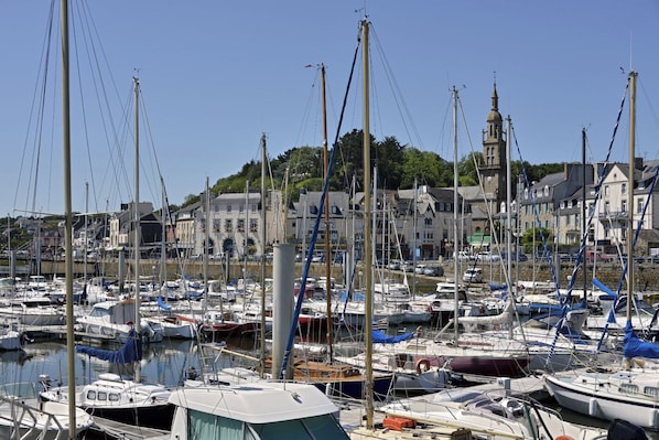 Ein Yachthafen mit zahlreichen vor Anker liegenden Booten, ein markantes Gebäude mit einem Turm und ein Hügelgrün im Hintergrund.
