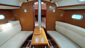 A boat interior with two cushioned seating areas, a central table, and a window.