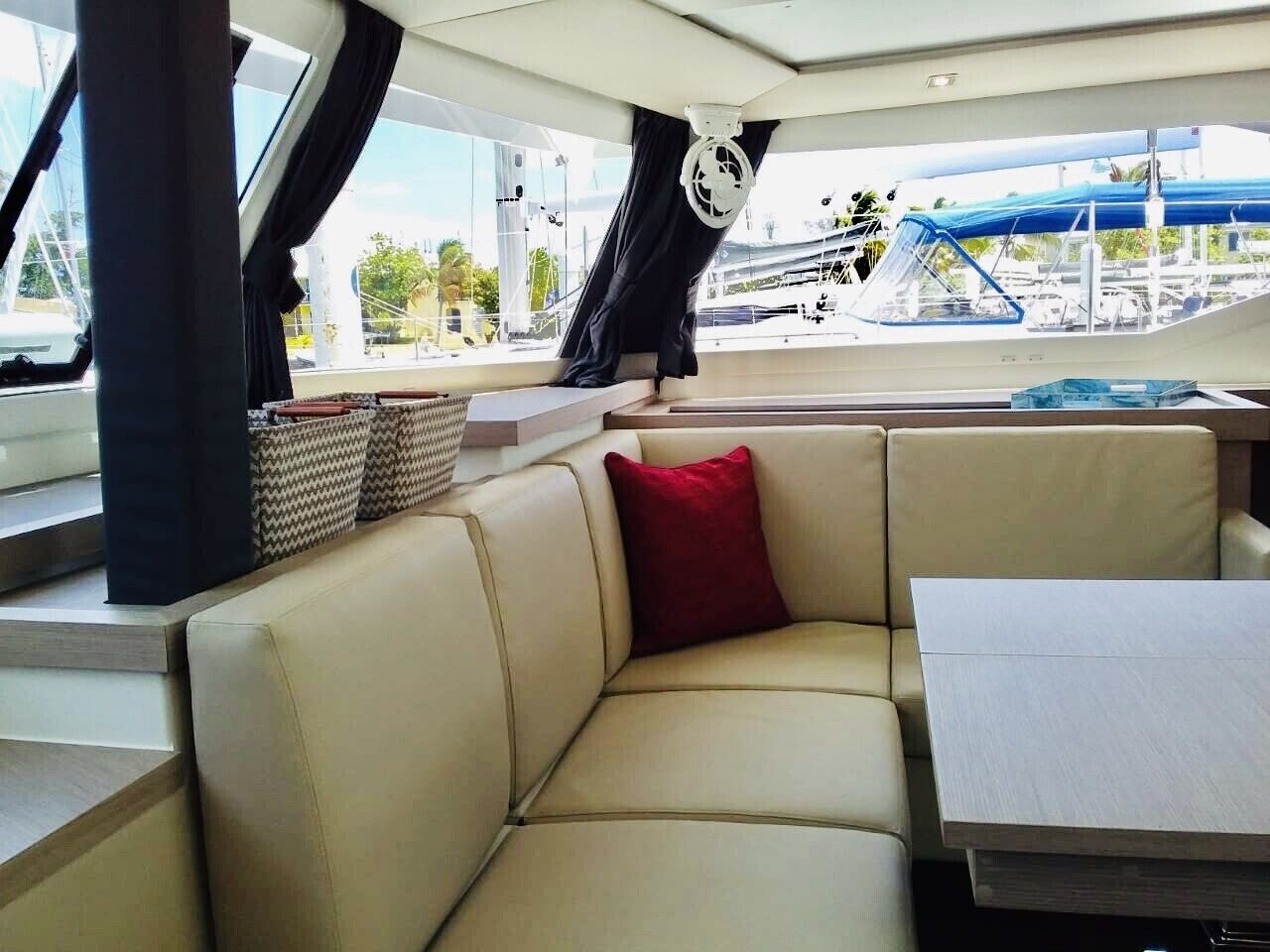 L'intérieur d'un bateau, avec un espace salon doté de sièges rembourrés, une table et une vue sur le port de plaisance.