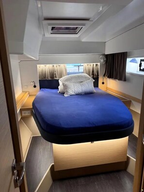 A compact, well-lit bedroom with a bed, bedside table, and a window with curtains.