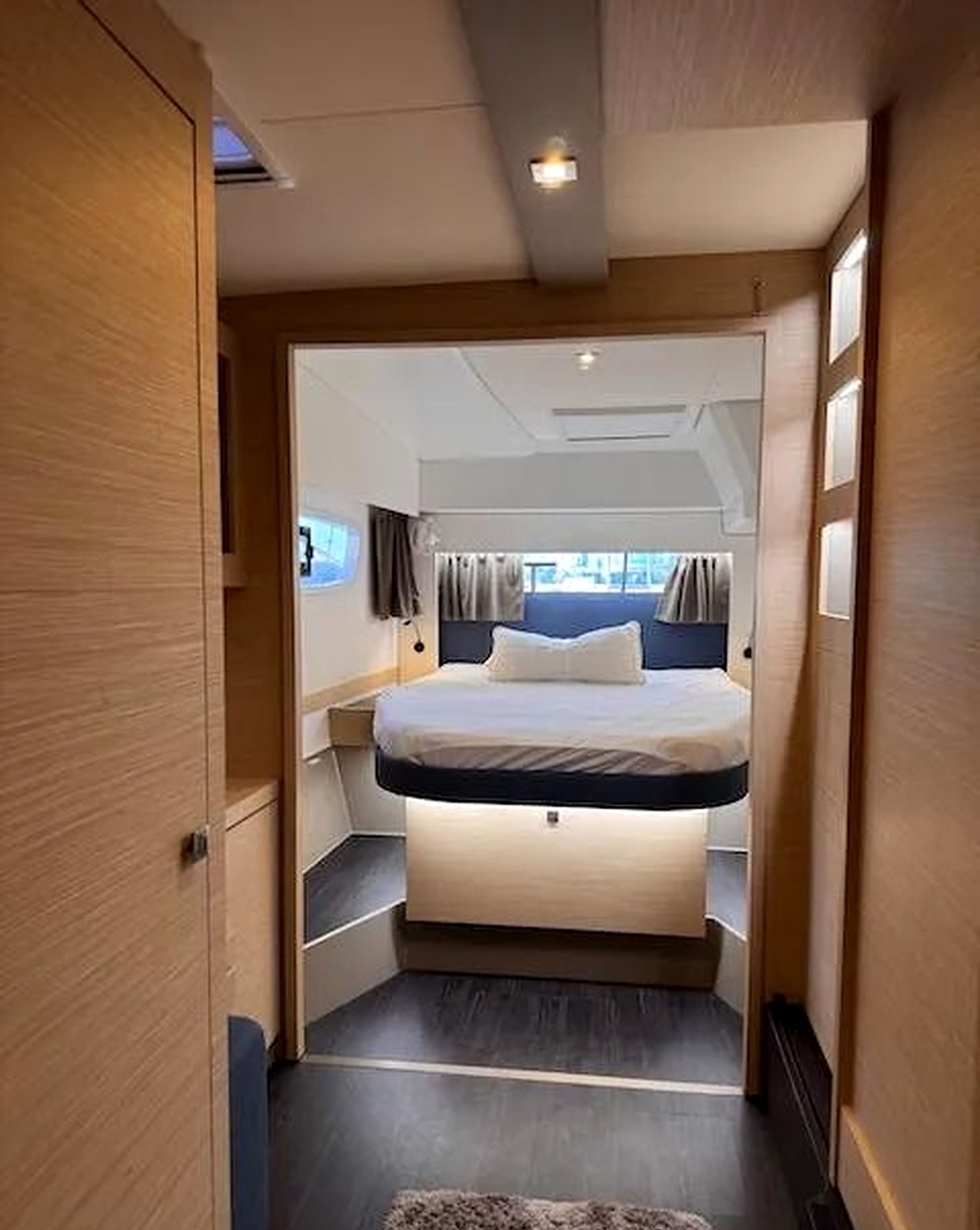 A narrow hallway leading to a room with a bed, a window, and a view of the outside.