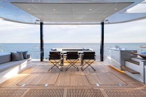 A deck with a table and chairs, a sofa with cushions, and a view of the sea. - Sun-Kissed Sailing Adventure in Islas Sarónicas (Alimos)