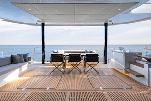 A deck with a table and chairs, a sofa with cushions, and a view of the sea. - Sun-Kissed Sailing Adventure in Islas Sarónicas (Alimos)