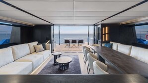 Un interno moderno con un divano, un tavolo da pranzo e sedie, vista sul mare attraverso ampie finestre.