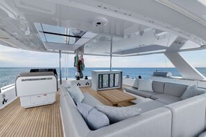 A yacht interior with a wooden deck, a seating area with cushions, a table, and a view of the sea. - Sun-Kissed Sailing Adventure in Islas Sarónicas (Alimos)