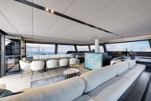 A modern yacht interior with a dining area, seating, and a control station. - Sun-Kissed Sailing Adventure in Islas Sarónicas (Alimos)