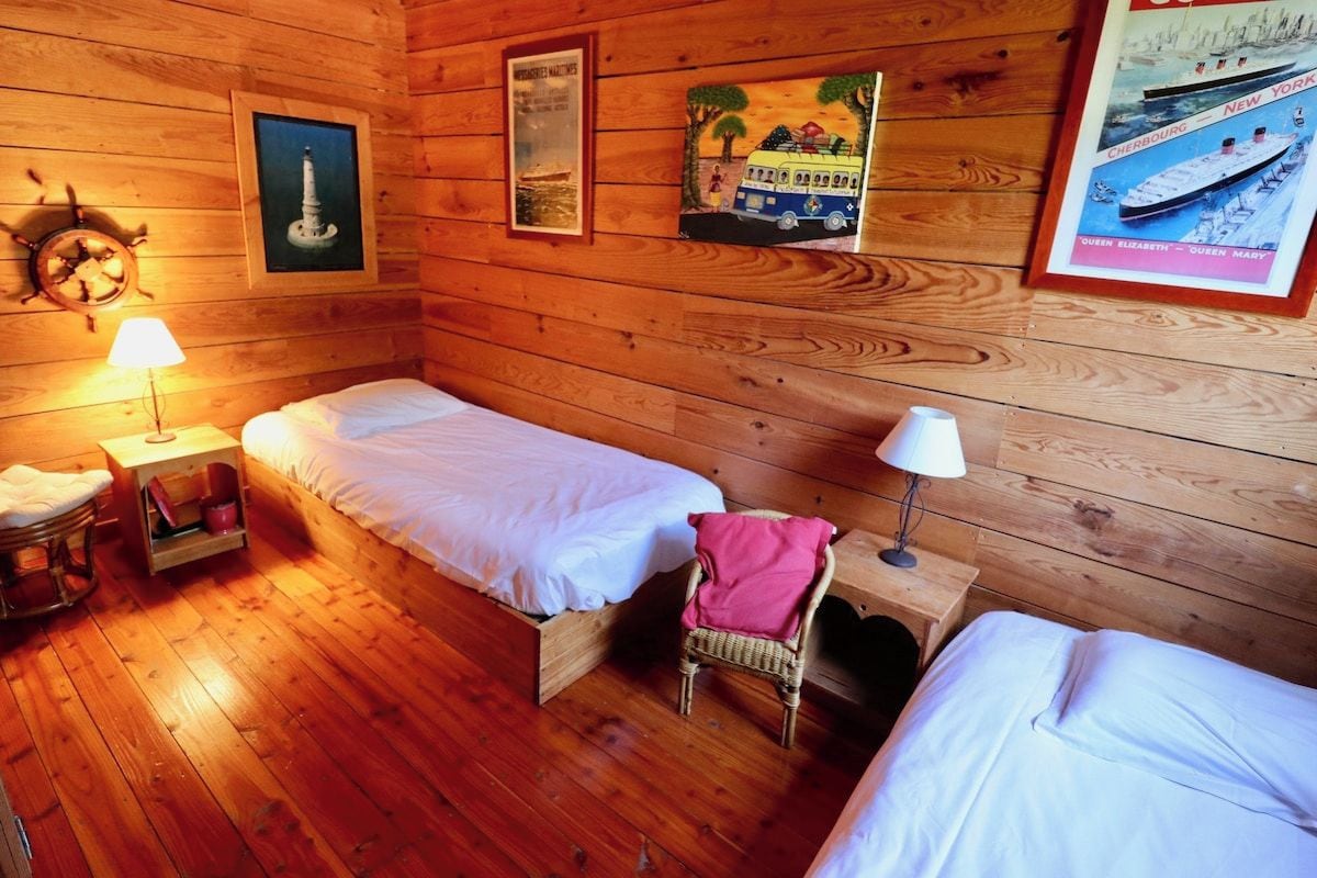 Una cabina con due letti singoli, una parete in legno, una ruota di timone e quadri appesi.