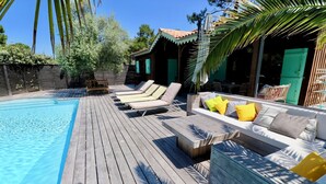 Una terraza de madera con piscina, sillones de descanso y un sofá con cojines.