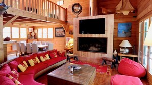 Ein Holzblockhaus-Interieur mit Essbereich, einem Wohnzimmer mit Sofa und Couchtisch, einem Kamin und einem Balkon mit Geländer.