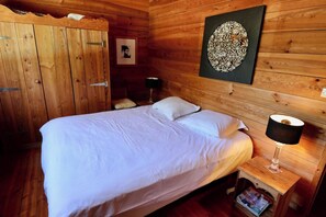 A wooden room with a bed, a nightstand with a lamp, a framed picture, and a wall decoration. - Charming villa with pool & idyllic terrace A3691 (Lège-Cap-Ferret)