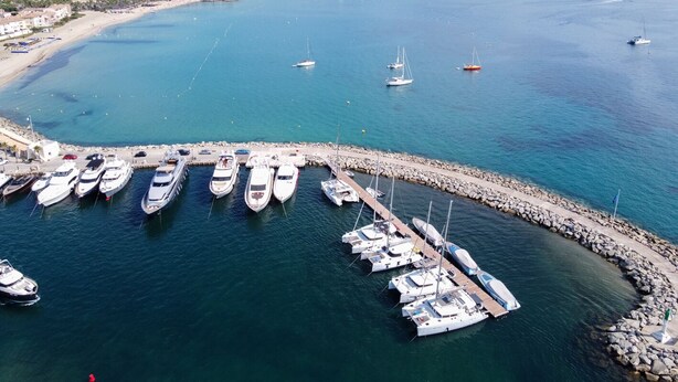 A marina with boats docked, a rocky breakwater, and a coastal town in the background. - Sun-Kissed Sailing Adventure in Provence-Alpes-Côte d'Azur (Cogolin)