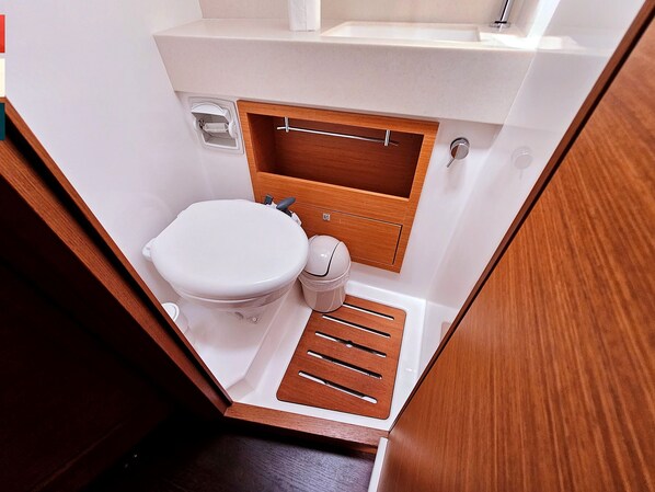 A compact bathroom with a toilet, a small sink, and a wooden vanity.