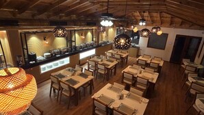 Un restaurante con mesas y sillas de madera, iluminación colgante y una barra con productos alimenticios.