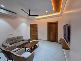 Una sala de estar moderna con un conjunto de sofá, una mesa de centro, un ventilador de techo y un televisor montado en la pared.