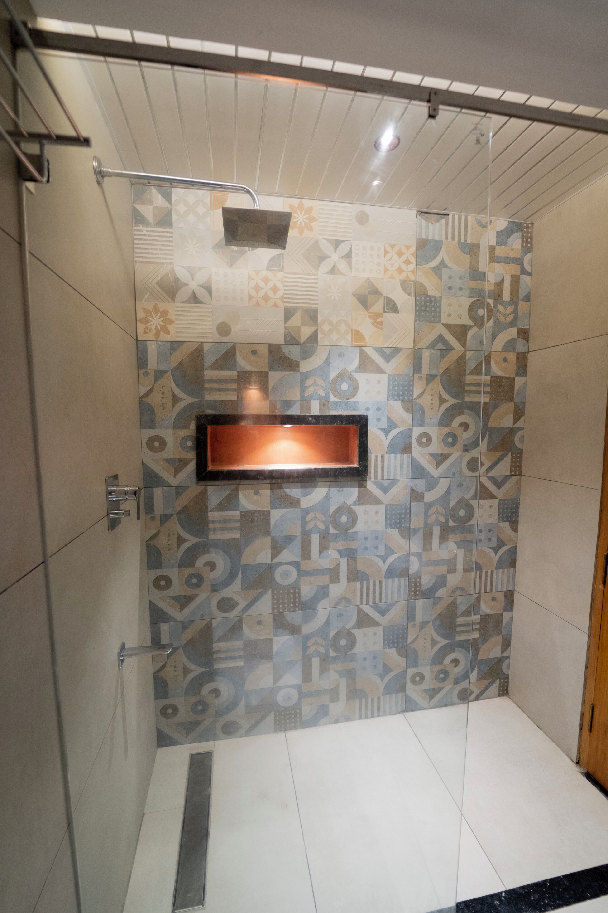 Une douche avec un carrelage aux motifs géométriques, une barre d’appui en métal et un miroir rectangulaire.