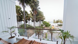 Un balcón con sillas de madera, plantas en macetas y vistas a palmeras y una playa.