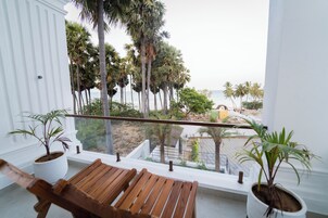 Un balcón con sillas de madera, plantas en macetas y vistas a palmeras y una playa.