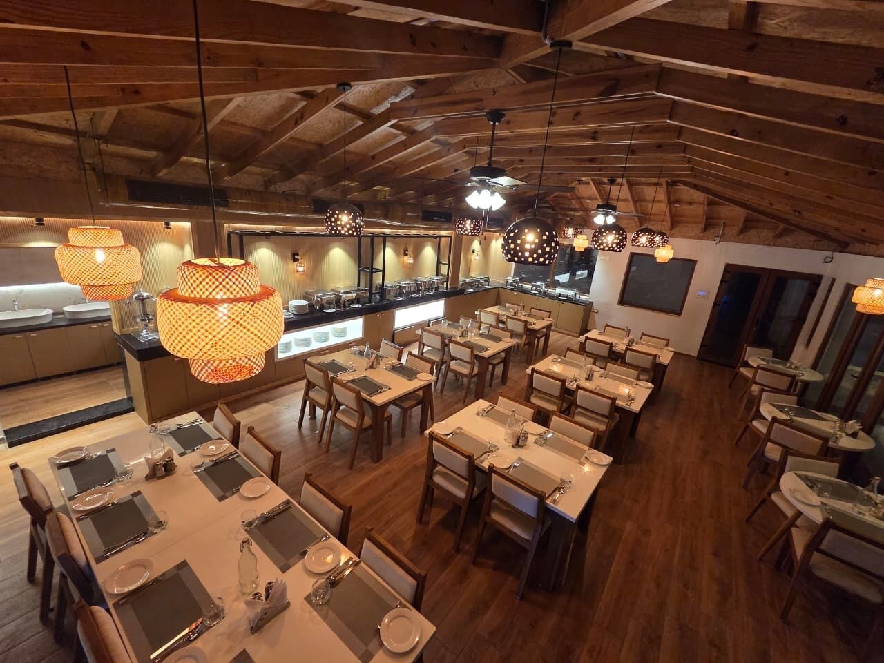 A restaurant with wooden ceilings, round tables, and hanging lamps.