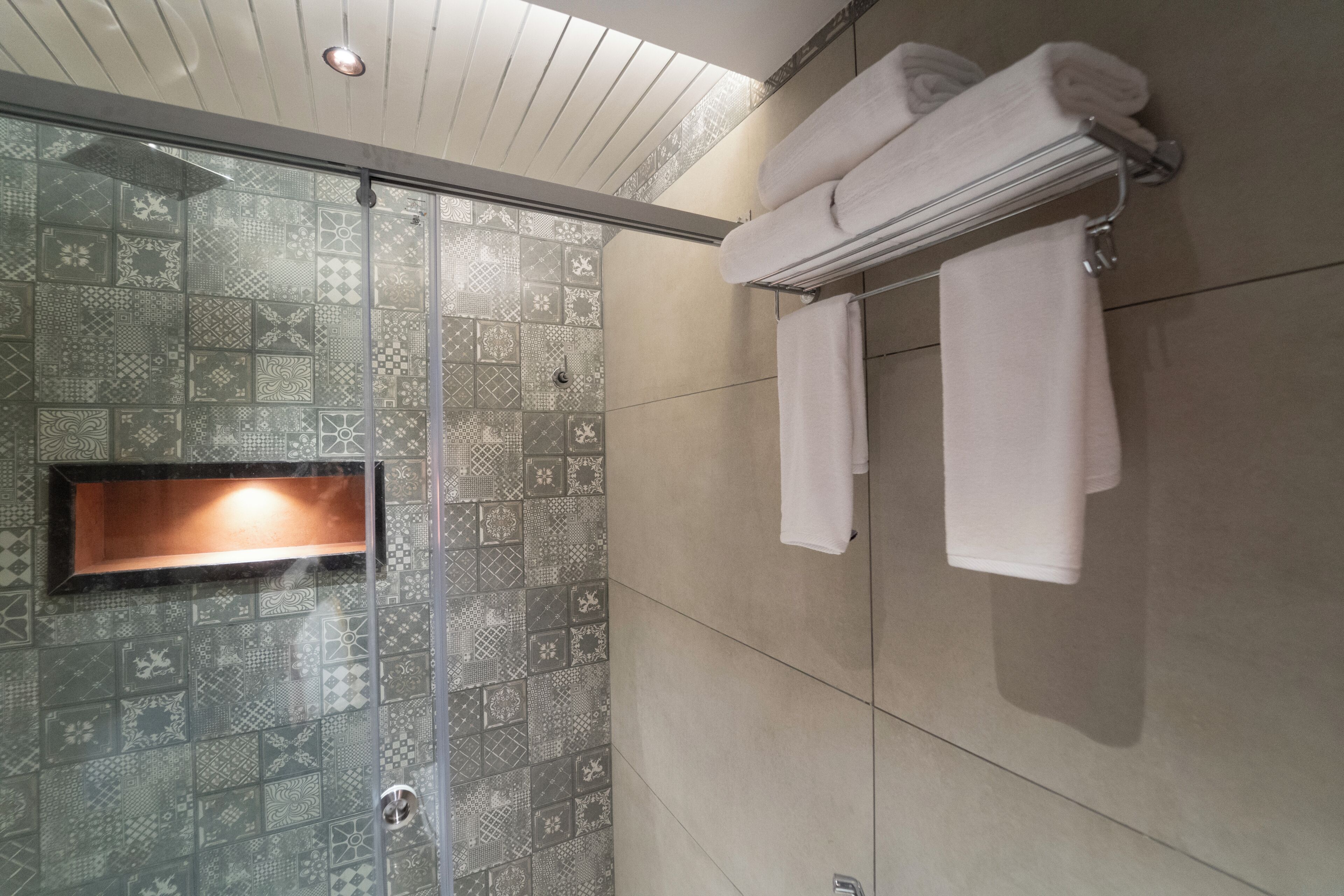 A shower with patterned tiles, a glass door, and a towel rack with folded towels.