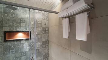 A shower with patterned tiles, a glass door, and a towel rack with folded towels.