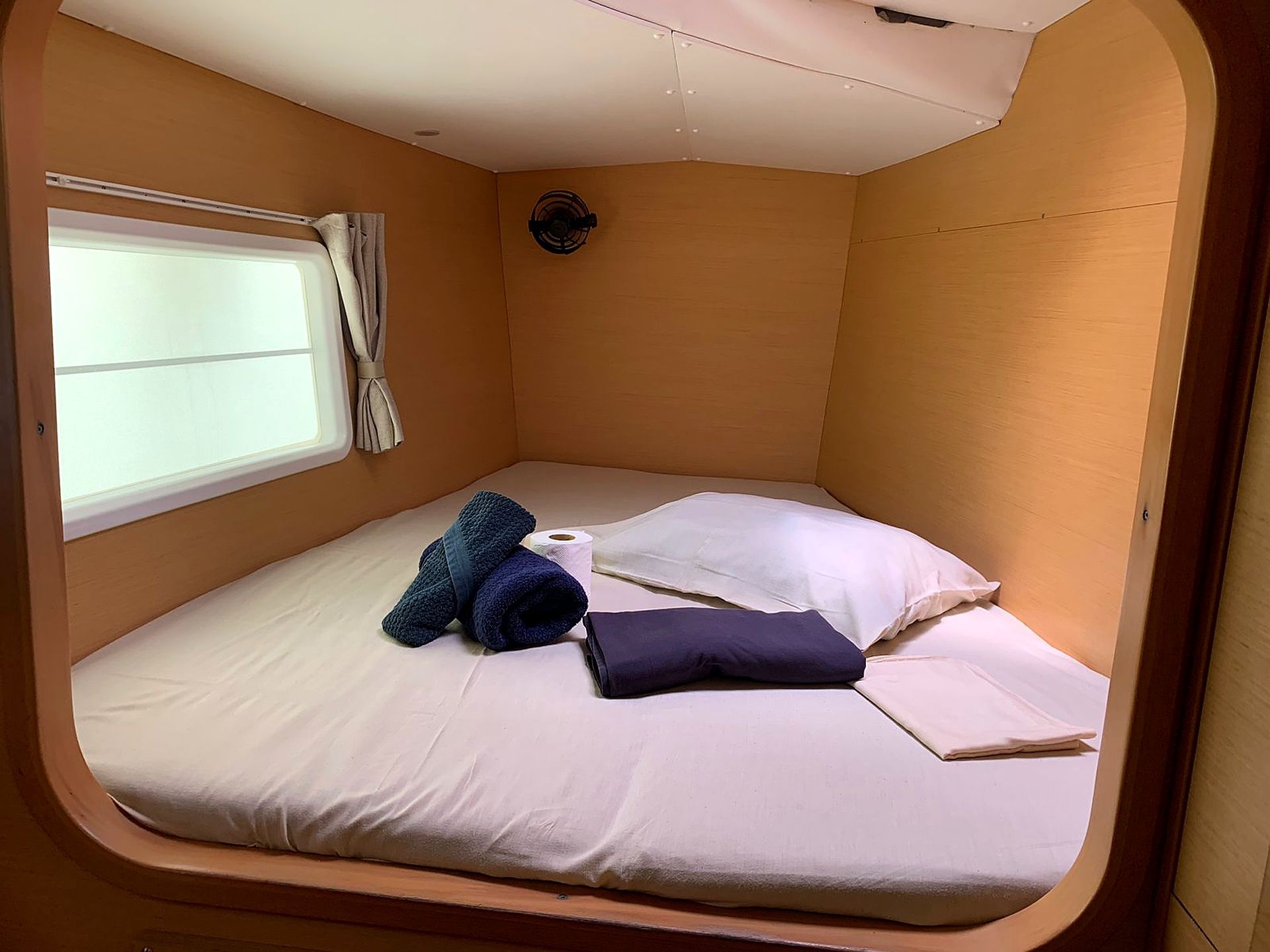 Una habitación pequeña con una cama individual, una ventana con cortinas y un ventilador de techo.