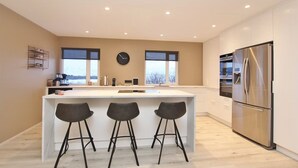 Una cocina moderna con una isla central, taburetes de bar, un refrigerador de acero inoxidable y un reloj en la pared.