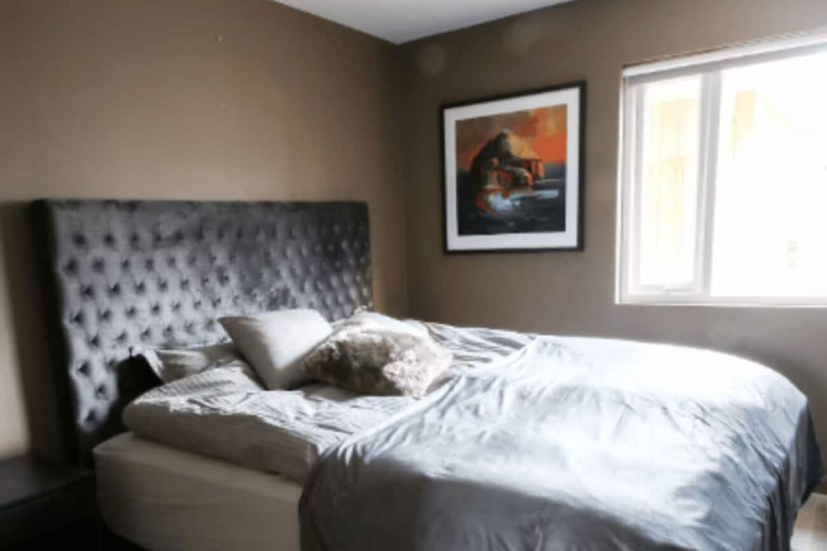 A bedroom with a bed, a headboard, a window, and a painting on the wall.