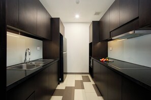 A narrow kitchen with dark cabinetry, a stainless steel sink, and a tiled floor. - Queens Flower Village Danang (NGũ hành sơn)